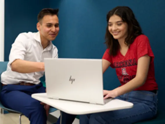 Two students sitting in front of a desk and talking.