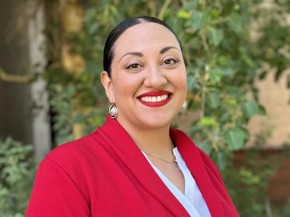Michelle McKelvey in a red blazer in front of foliage. 