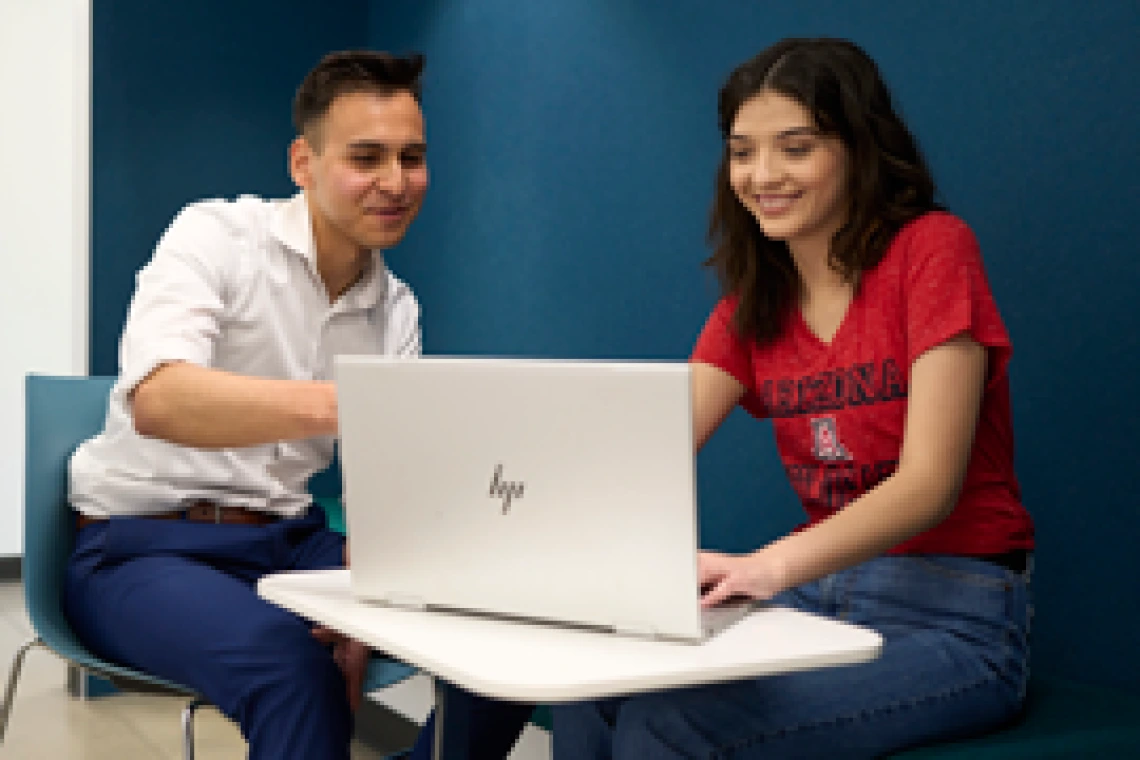 Two students sitting in front of a desk and talking.