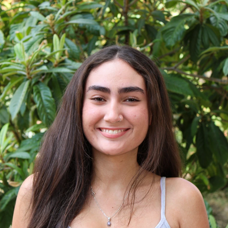 Lia Lopez-Ruelas. Smiling at the camera with a green foliage background.