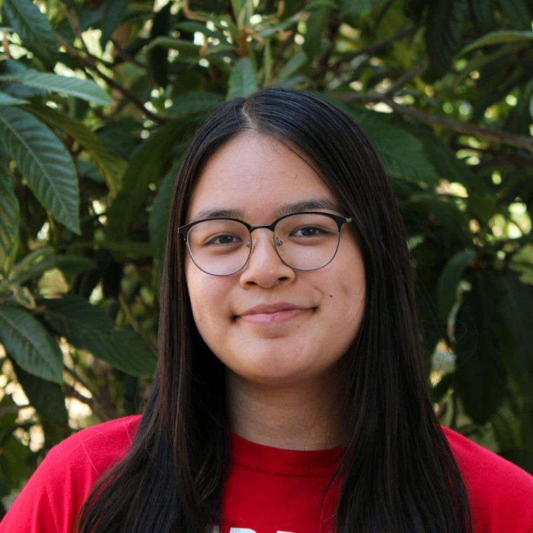 Jazlynn Do Le, wearing a red t-shirt. Smiling posing to the camera with a green foliage background.
