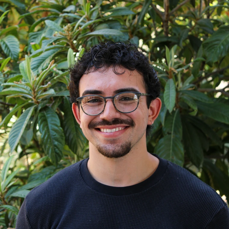 Ernesto Jacobo, wearing a black t-shirt and glasses in front of a green foliage background