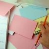 Image of a desk with a notebook and flashcards.  Hand at bottom right with a pencil between thumb and middle finger.